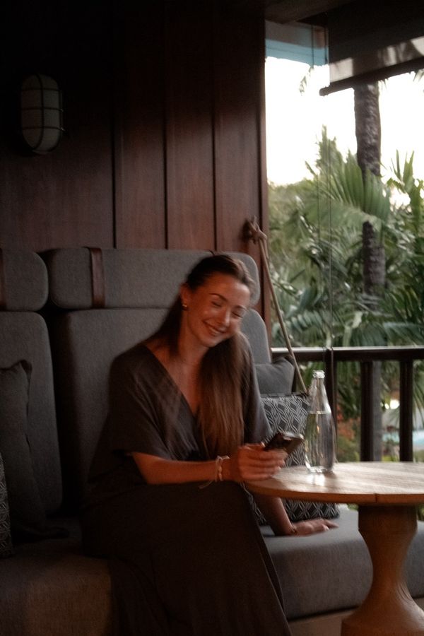 Maxima sitzt lächelnd auf einer Couch und schaut auf ihr Handy